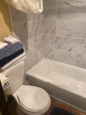 Une salle de bain avec des toilettes blanches, une baignoire et un mur recouvert de carreaux de marbre.