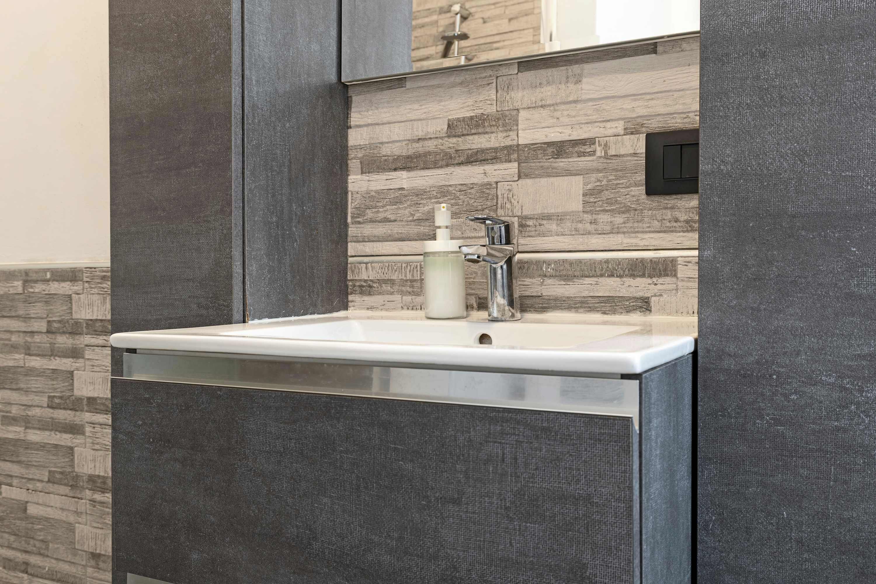 Un baño con un lavamanos moderno, un espejo y un reverso de madera.