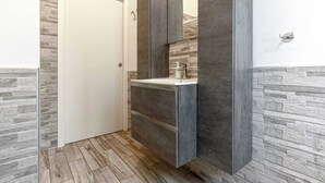 A bathroom with a wooden floor, a white sink, and a dark cabinet.