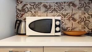 A microwave oven, a kettle, and a bowl on a kitchen counter with patterned tiles in the background.