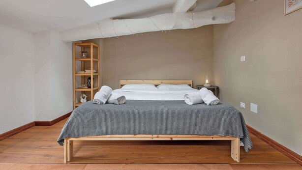 Ein Schlafzimmer mit Oberlicht, einem Holzbettgestell, einem Nachttisch mit Lampe und einer Holzregaleinheit.