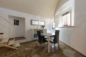 A dining area with a table and chairs, a staircase, a shelf with decorative items, and a window with curtains.