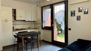 A compact kitchen with a dining table and chairs, a sofa, and a sliding glass door leading to a garden.