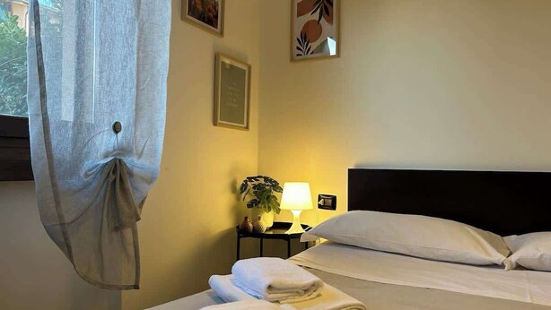 A hotel room with two beds, a nightstand with a lamp, and a window with a curtain.
