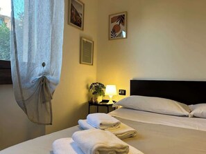 Habitación de hotel con dos camas, una mesita de noche con lámpara y una ventana con cortina.