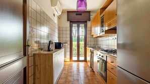 Eine schmale Küche mit Holzschränken, einem Edelstahlkühlschrank und Blick ins Freie.