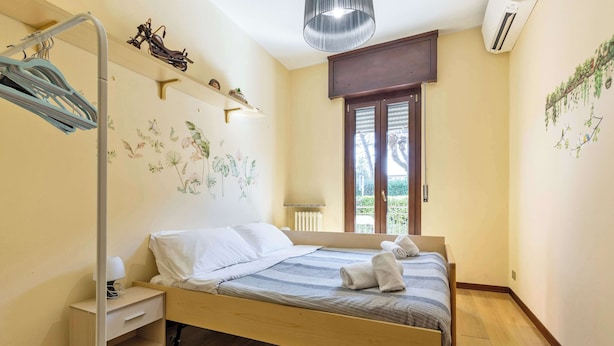 Ein Schlafzimmer mit Bett, Nachttisch, Wandregal, Heizkörper und Fenster mit Blick.