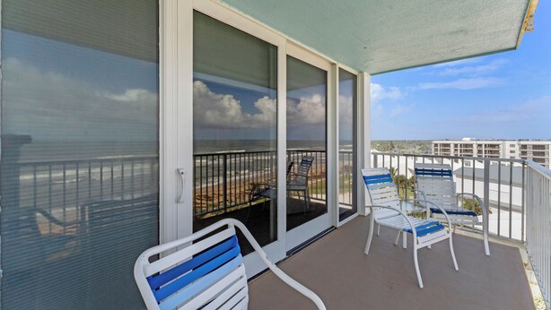 Ein Balkon mit Blick auf den Strand, eine Glastür und zwei Stühle.