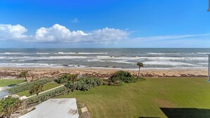 Eine Küstenansicht mit einer grünen Wiese, einem Strand und dem Meer.
