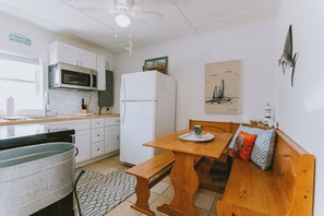 Kompakti keittiö, jossa on valkoiset kaapit, mikroaaltouuni, jääkaappi ja puinen ruokapöytä penkeillä.