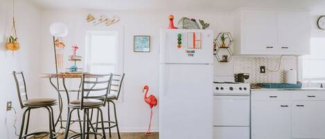 A kitchen with white cabinets, a white refrigerator, a stove, and a dining area with chairs and a table.