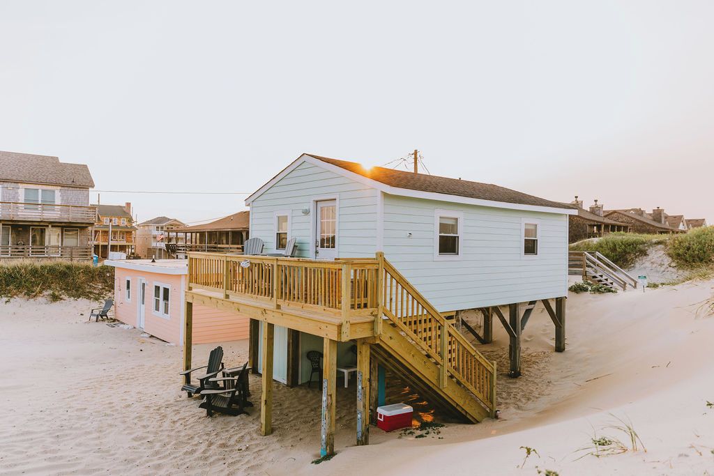 Une maison de plage dotée d’une terrasse en bois et d’un escalier menant au bâtiment principal.