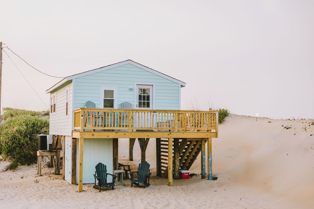 A beach house with a wooden deck, two chairs, and a small table.