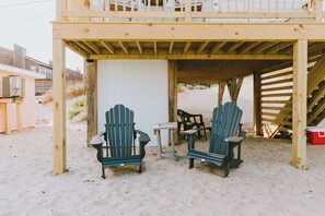 A wooden deck with two Adirondack chairs and a small table, overlooking a sandy beach area. - Coastal Dunes 1: Oceanfront Cottage in Nags Head, Great Views! (Nags Head)