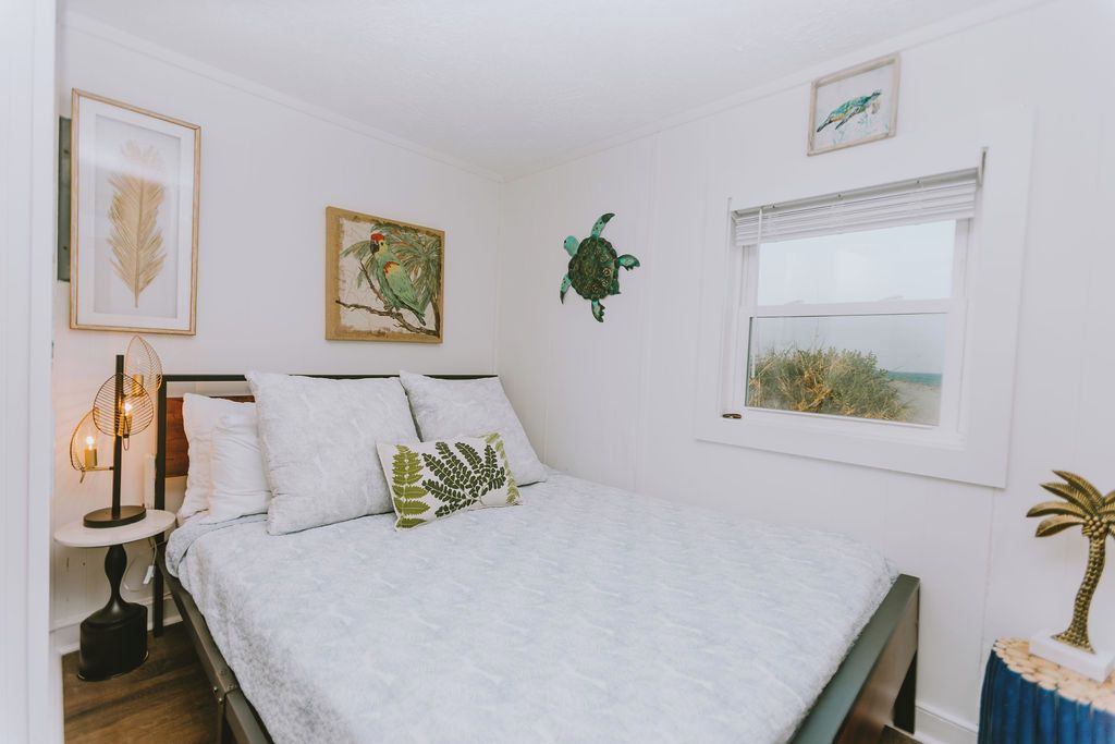 Un dormitorio con una cama, una mesita de noche con lámpara, y detalles decorativos en la pared como un pájaro, una tortuga y una planta.