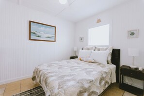 A bedroom with a bed, a nightstand, a window, and a wall-mounted picture.