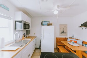 Een compacte keuken met witte kastjes, een magnetron, een koelkast en een eethoek met een houten tafel en bankjes.