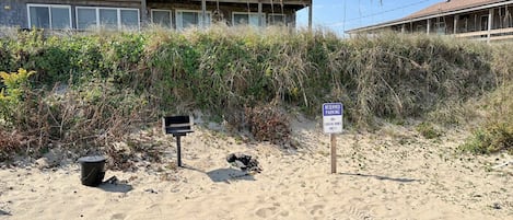 A beachfront property with a two-story building, a reserved parking sign, and a trash bin.