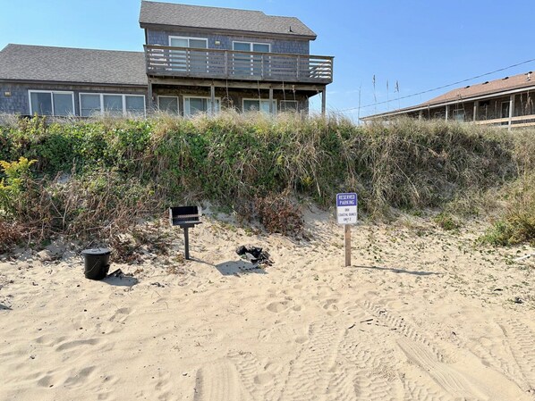 Una propiedad frente a la playa con un edificio de dos pisos, un letrero de estacionamiento reservado y un basurero.