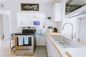 A modern kitchen with white cabinetry, a stainless steel stove, a sink, and a chalkboard sign above the stove.