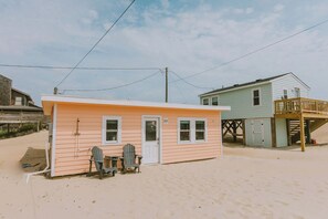 Et lille strandhus med en dør og to vinduer, samt en terrasse og en stol udenfor.