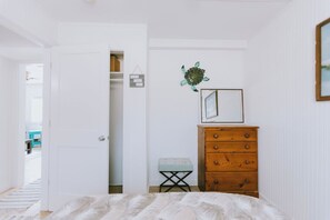 Un dormitorio con una cama, un aparador de madera, un taburete pequeño y un adorno en la pared.