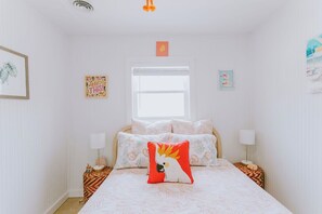 Ein Schlafzimmer mit einem Bett, zwei Nachttischen, einem Fenster und Wandbildern.