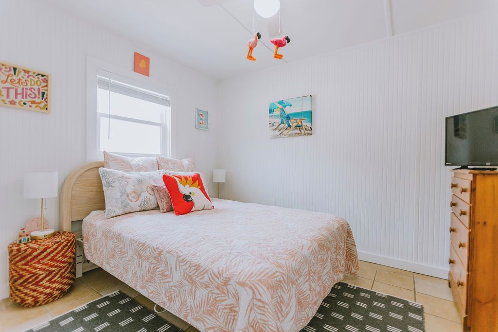 A bedroom with a bed, a television, a window, and a wall with a picture.