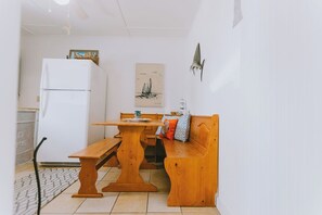 Una cocina compacta con un refrigerador blanco, asientos tipo banca de madera y piso de baldosas.