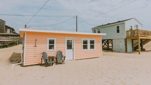 A small beach house with a single door and two windows, a deck, and a chair outside. - Coastal Dunes 2: Pet Friendly, Oceanfront Cottage in Nags Head (Nags Head)