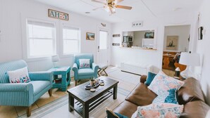 A bright living room with a ceiling fan, a kitchen in the background, and a sign that reads "AHOY". - Coastal Dunes 2: Pet Friendly, Oceanfront Cottage in Nags Head (Nags Head)