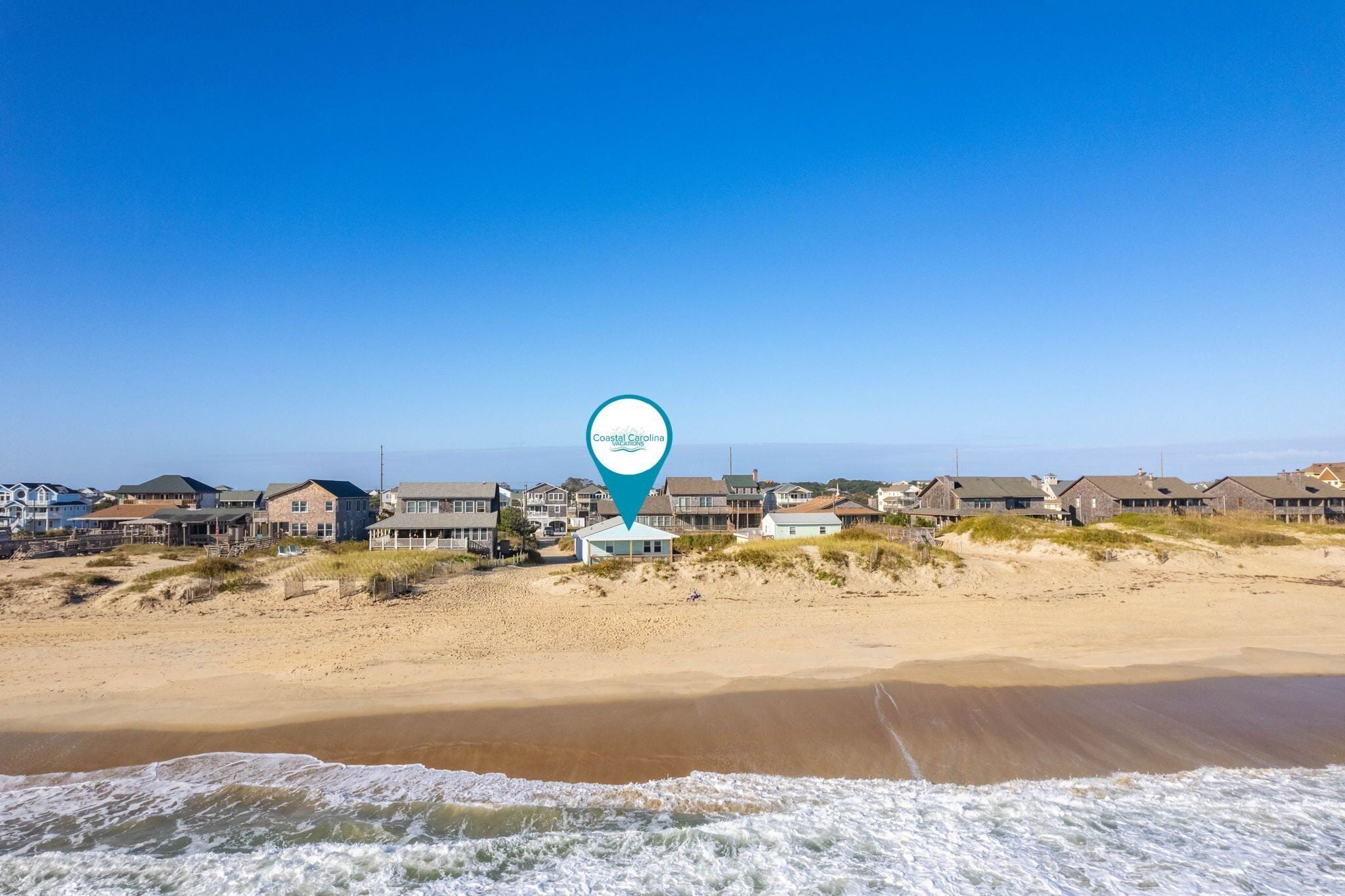 Une vue d’une plage côtière avec des maisons et un marqueur de localisation.