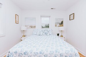 A bedroom with a large bed, white walls, and two bedside tables with lamps. - Coastal Dune 3: Oceanfront Cottage on the Sand in Nags Head! (Nags Head)