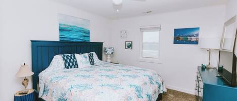 Un dormitorio con cama, ventilador de techo, ventana y cómoda.