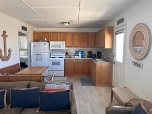 A compact kitchen with wooden cabinets, a refrigerator, microwave, stove, and a coffee maker. - Coastal Dune 3: Oceanfront Cottage on the Sand in Nags Head! (Nags Head)