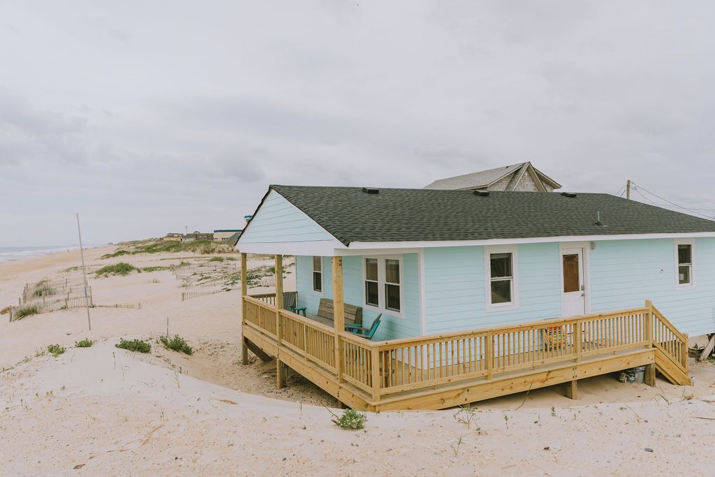A light blue beach house with a wooden deck and a covered porch.