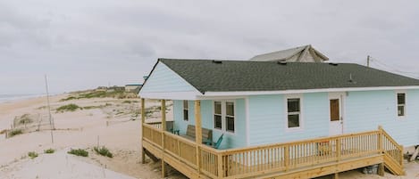 A light blue beach house with a wooden deck and a covered porch.