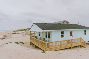 Une maison de plage bleu clair avec une terrasse en bois et un porche abrité.