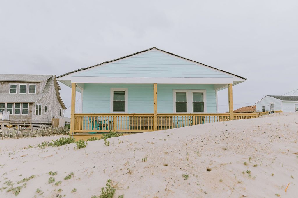 A beach house with a light blue exterior, a wooden deck, and a sloped roof.