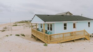 A light blue beach house with a wooden deck and a covered porch.