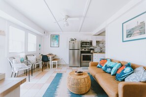 Un espace de vie compact comprenant un coin cuisine, un coin repas et un espace détente avec un canapé et des fauteuils.