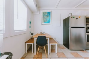 A compact kitchen with a wooden table, a black chair, and a stainless steel refrigerator. - Coastal Dune 4: Pet-Friendly, Cottage on the Beach in Nags Head (Nags Head)