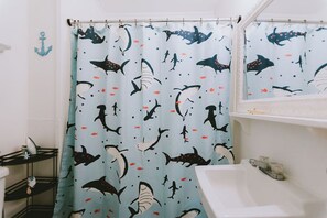 A bathroom with a shower curtain featuring a shark and fish pattern, a white sink, and a mirror above the sink. - Coastal Dune 4: Pet-Friendly, Cottage on the Beach in Nags Head (Nags Head)