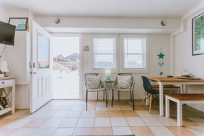 Une pièce comprenant un coin repas, deux chaises, une table, un téléviseur et une porte donnant sur l’extérieur.