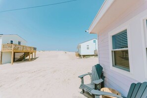 Una casa de playa con un balcón y un pequeño porche, ubicada en una playa arenosa.