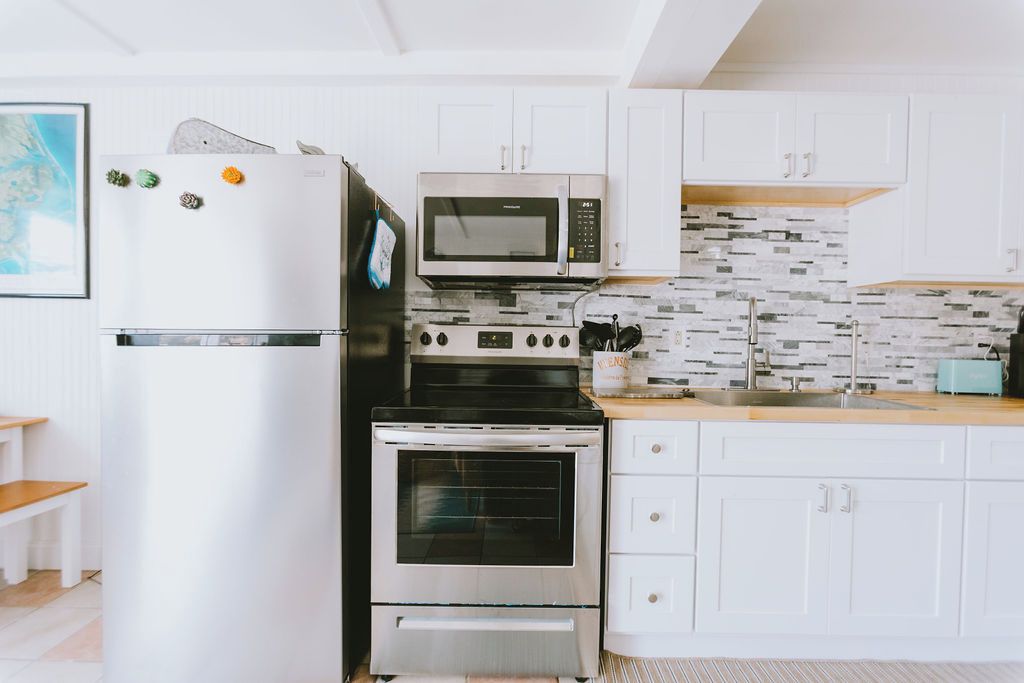 A kitchen with white cabinets, a stainless steel refrigerator, a microwave, an oven, and a tiled backsplash.