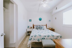 Un dormitorio con cama, mesitas de noche, ventilador de techo y ventana.