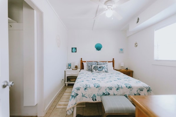 A bedroom with a bed, bedside tables, a ceiling fan, and a window.