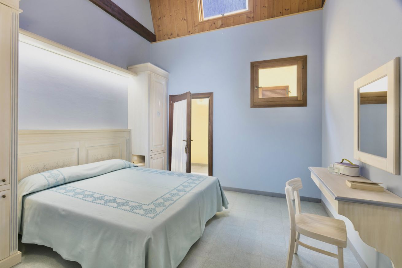 Un dormitorio con cama, escritorio, silla, armario y ventana.