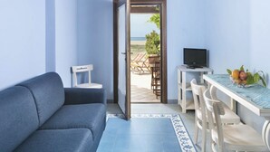 A room with a sofa, a dining table with chairs, a TV, and a view of the beach. - Nice apartment on the ground floor with sea view of about 45 m2 equipped with air conditioning and wi fi connection, composed of a living room with equipped kitchenette, fridge and flat-screen television.It can be on one level or with a mezzanineA double (Bosa Marina)